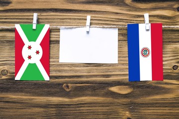 Hanging flags of Burundi and Paraguay attached to rope with clothes pins with copy space on white note paper on wooden background.Diplomatic relations between countries.