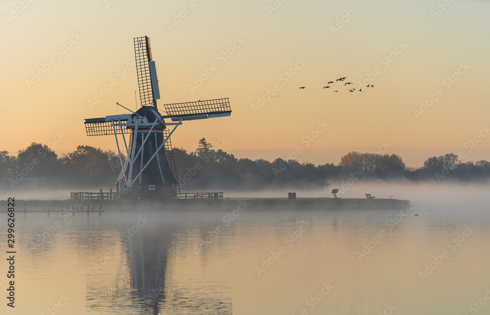 Nature awakens at a traditional Dutch windmill during a foggy sunrise. De Helper, Groningen. - obrazy, fototapety, plakaty 