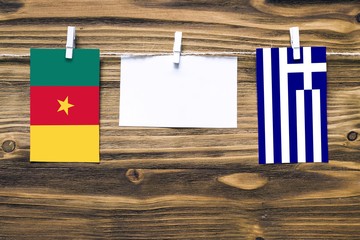 Wall Mural - Hanging flags of Cameroon and Greece attached to rope with clothes pins with copy space on white note paper on wooden background.Diplomatic relations between countries.