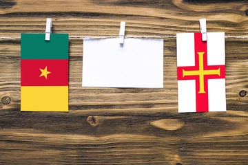 Wall Mural - Hanging flags of Cameroon and Guernsey attached to rope with clothes pins with copy space on white note paper on wooden background.Diplomatic relations between countries.