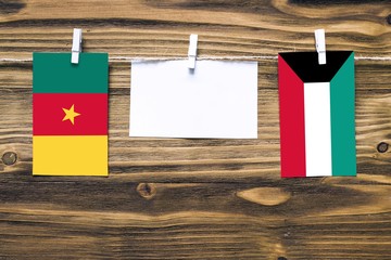 Wall Mural - Hanging flags of Cameroon and Kuwait attached to rope with clothes pins with copy space on white note paper on wooden background.Diplomatic relations between countries.