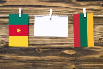 Wall Mural - Hanging flags of Cameroon and Lithuania attached to rope with clothes pins with copy space on white note paper on wooden background.Diplomatic relations between countries.