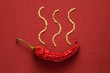 Single red dried banana pepper on a red paper background with pepper seeds