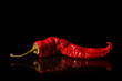 Single red dried banana pepper on a black background with a reflection