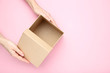 Female hands opening brown gift box on pink background
