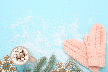 Poster - Knitted mittens with snowflakes and cup of hot drink on blue background