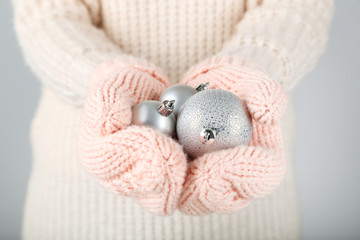 Poster - Hands in knitted mittens holding christmas baubles on grey background