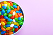 Bowl with colorful jelly beans on lilac background, top view. Space for text