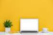 © New Africa - Modern laptop on desk near yellow wall, space for design. Home workplace