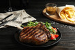 Tasty grilled beef steak with salad on black wooden table