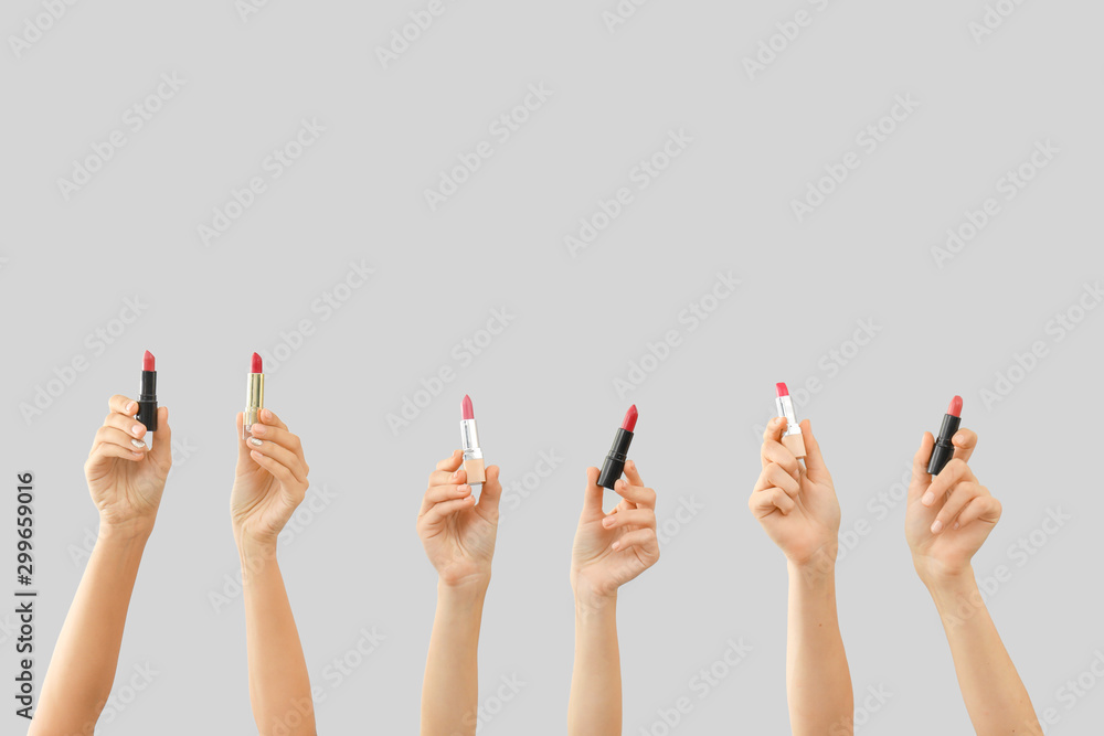 Many hands with lipsticks on grey background