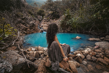 Wall Mural - Beautiful young woman sitting at small mountain lake