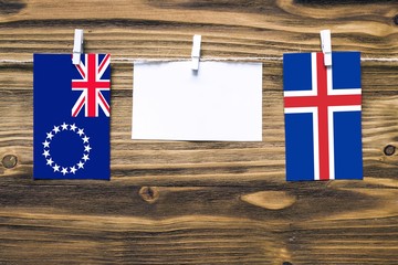 Wall Mural - Hanging flags of Cook Islands and Iceland attached to rope with clothes pins with copy space on white note paper on wooden background.Diplomatic relations between countries.