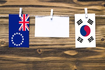 Wall Mural - Hanging flags of Cook Islands and South Korea attached to rope with clothes pins with copy space on white note paper on wooden background.Diplomatic relations between countries.