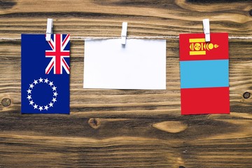 Wall Mural - Hanging flags of Cook Islands and Mongolia attached to rope with clothes pins with copy space on white note paper on wooden background.Diplomatic relations between countries.