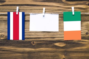 Wall Mural - Hanging flags of Costa Rica and Ireland attached to rope with clothes pins with copy space on white note paper on wooden background.Diplomatic relations between countries.