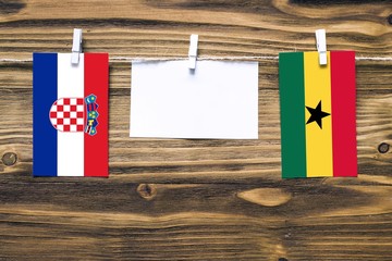 Hanging flags of Croatia and Ghana attached to rope with clothes pins with copy space on white note paper on wooden background.Diplomatic relations between countries.