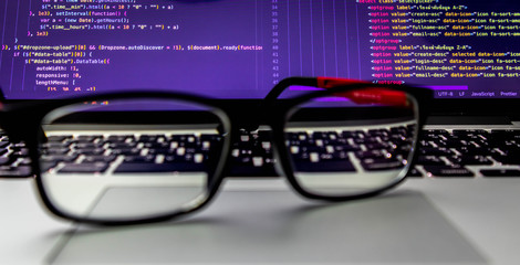 Glasses placed on the laptop At the back is the screen of the program source code. That programmers can develop into websites or mobile apps Which system analysts and designers have designed
