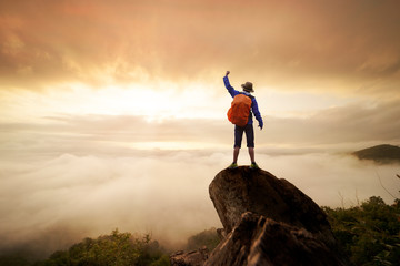 Backpacker man raise hand up on top of mountain with sun sky and fog backgeound