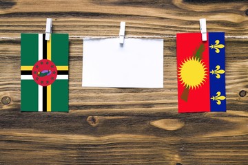 Hanging flags of Dominica and Guadeloupe attached to rope with clothes pins with copy space on white note paper on wooden background.Diplomatic relations between countries.