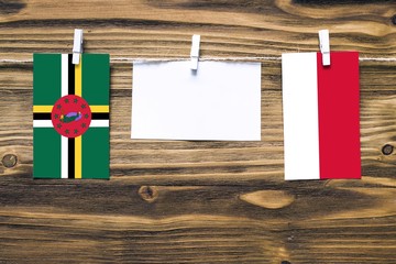 Hanging flags of Dominica and Monaco attached to rope with clothes pins with copy space on white note paper on wooden background.Diplomatic relations between countries.