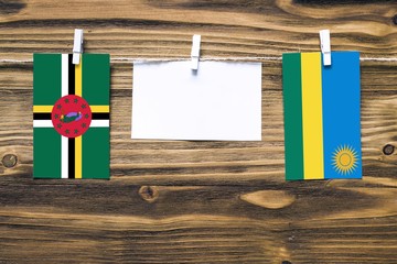 Hanging flags of Dominica and Rwanda attached to rope with clothes pins with copy space on white note paper on wooden background.Diplomatic relations between countries.