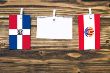 Hanging flags of Dominican Republic and French Polynesia attached to rope with clothes pins with copy space on white note paper on wooden background.Diplomatic relations between countries.