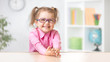 © Andrey Kuzmin - Happy kid girl in eyeglasses sitting at table