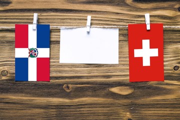 Hanging flags of Dominican Republic and Switzerland attached to rope with clothes pins with copy space on white note paper on wooden background.Diplomatic relations between countries.