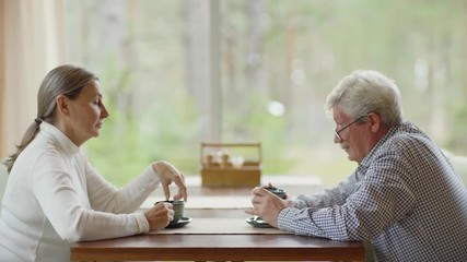 Wall Mural - Side view zoom in shot of senior man and woman sitting at table in cafe and talking over tea or coffee