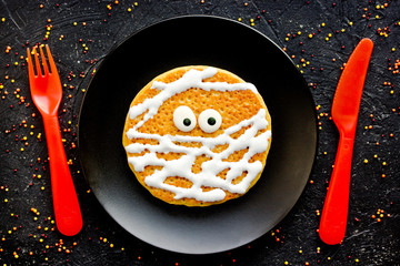 Wall Mural - Mummy pancake , funny idea for kids for Halloween breakfast , pumpkin pancake with cream and candy eyes shaped mummy on black plate top view