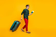 Full length body size side profile photo of man carrying his baggage holding passport and tickets to get on board walking towards airplane in red pants trousers isolated vivid color yellow background