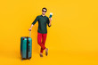 © deagreez - Full length photo of positive cheerful brunet hair guy feel content ready to travel voyage hold trolley tickets wear youth outfit red pants trousers sneakers isolated bright color background