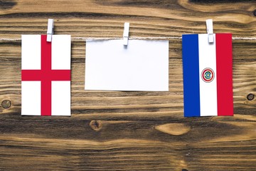 Hanging flags of England and Paraguay attached to rope with clothes pins with copy space on white note paper on wooden background.Diplomatic relations between countries.