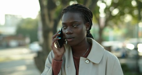 Wall Mural - Young african woman talking on the phone while sitting on the bench in the street