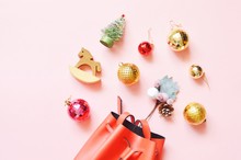 New Year Decoration And Gifts. Flat Lay Winter Holidays Items On A Light Pink Background. Christmas Tree, Wooden Horse, Red, Golden Balls And Red Bag