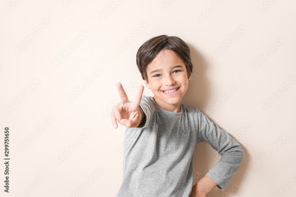 Happy little boy showing victory gesture on light background