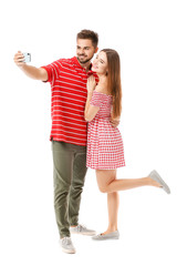 Portrait of happy young couple taking selfie on white background