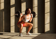 strong  sportswoman doing squats with barbell near concrete wall in gym, natural sun light