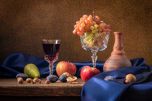 Still Life With Fruit And Red Wine. Grapes, Apples, Pear, Plums, Nuts And Blue Drapery