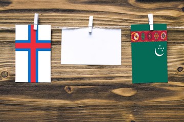 Hanging flags of Faroe Islands and Turkmenistan attached to rope with clothes pins with copy space on white note paper on wooden background.Diplomatic relations between countries.