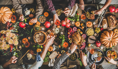 Wall Mural - Family celebrating Thanksgiving day. Flat-lay of eating and pouring wine peoples hands over Friendsgiving table with traditional Fall food, roasted turkey, candles, pumpkin pie, top view