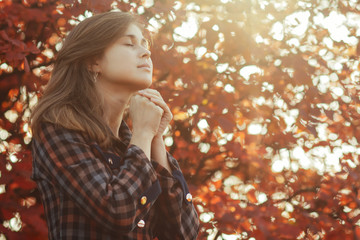 portrait of a young woman praying in nature, the girl thanks God with her hands folded at her chin, a conversation with the Creator, the concept of religion