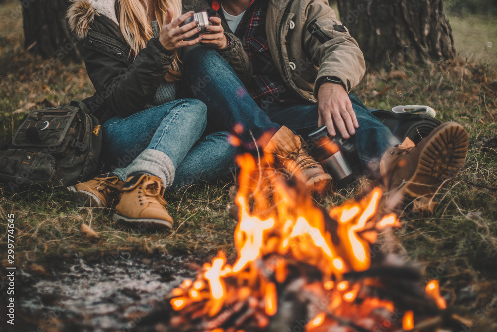 Traveler couple camping in the forest and relaxing near campfire after a hard day. Concept of trekking, adventure and seasonal vacation. - obrazy, fototapety, plakaty 