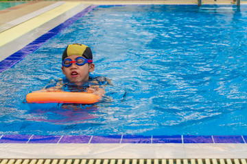 5 years old Lonely boy warm up with orange swimming kickboard before learning to swim in the blue swimming pools.