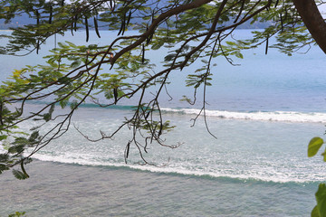 Wall Mural - sea waves roll on the sandy shore, foam and spray of water, against the backdrop of mountains and blue sky in the style of bounty