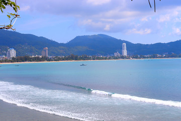 Wall Mural - sea waves roll on the sandy shore, foam and spray of water, against the backdrop of mountains and blue sky in the style of bounty