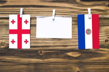 Hanging flags of Georgia and Paraguay attached to rope with clothes pins with copy space on white note paper on wooden background.Diplomatic relations between countries.