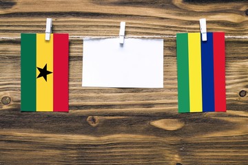 Hanging flags of Ghana and Mauritius attached to rope with clothes pins with copy space on white note paper on wooden background.Diplomatic relations between countries.