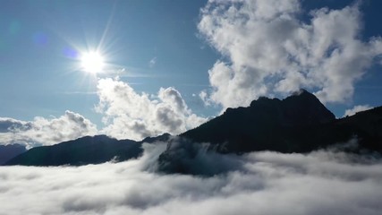 Wall Mural - aerial view of moving clouds, fog motion with sun and blue sky in austrian mountains